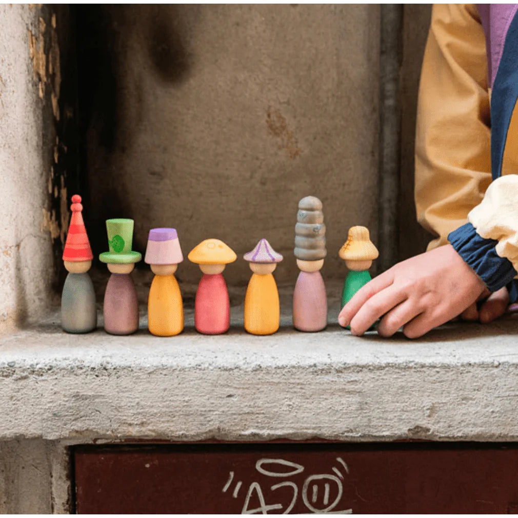 A child's hand arranging colorful, quirky Grapat Fancy Nins with interchangeable hats, set against a gray concrete background.
