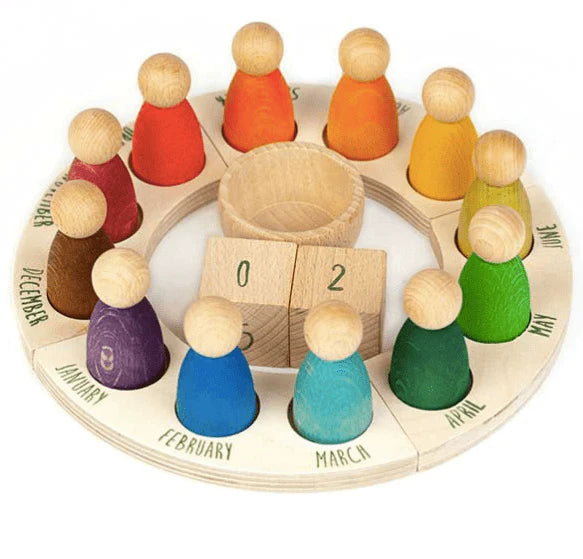The Grapat Perpetual Calendar with Peg Figures features a wooden annual calendar ring with a circular base, month labels, and 12 colorful peg dolls representing different months. The peg dolls are arranged around a central cup with numbers "0" and "2" visible.