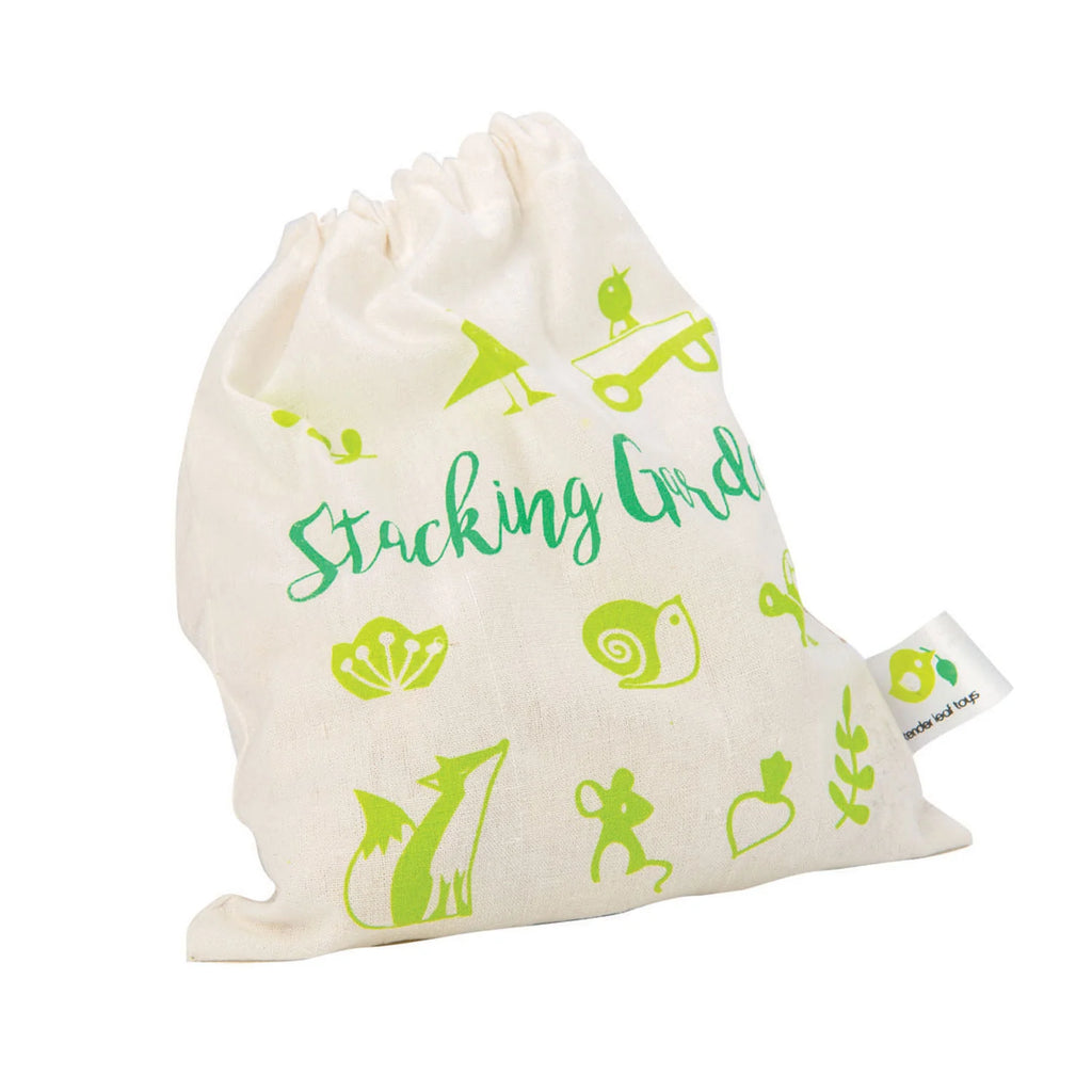 A white drawstring bag with green text saying "Stacking Garden Friends" and green illustrations of fruits, animals, and snacks designed for imaginative play. A small logo tag is visible on the side.