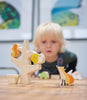 A young child with blonde hair, blurred in the background, intently observes Stacking Garden Friends arranged on a table, featuring a solid wood tree-shaped toy holder in focus.