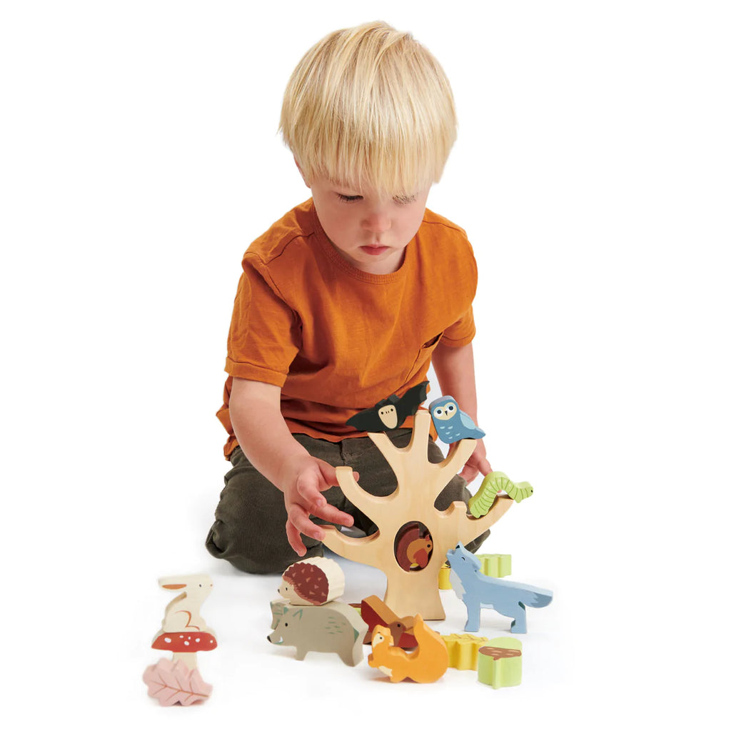A young child with blond hair is intently assembling a Stacking Forest puzzle with colored animals on a white background.