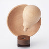 A Father's Factory Wooden Light Bulb Camera featuring a light bulb shape, resting in a wooden bowl with a separate round wooden base, displayed against a white background.