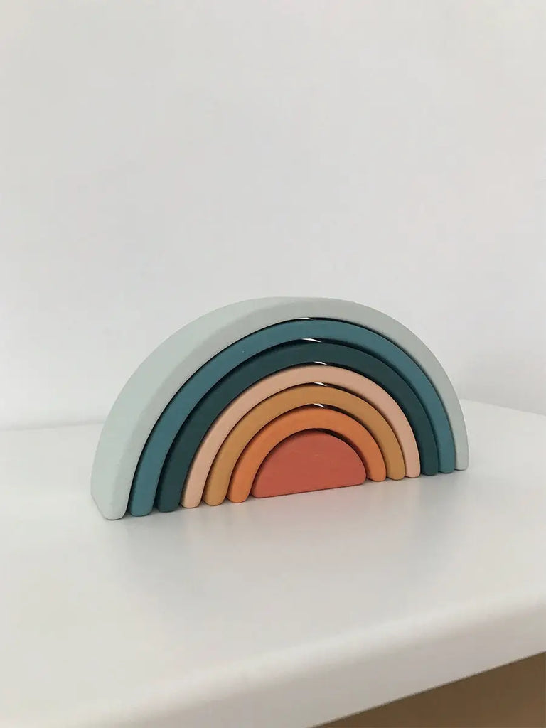 A Handmade Mini Rainbow Stacker - Lagoon in pastel colors, ranging from blue to pink, stacked in a curved, descending size order on a white surface against a white backdrop.