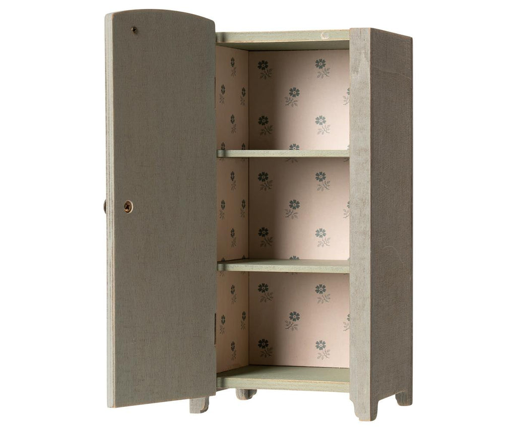 A small, freestanding Maileg Miniature Closet crafted from FSC-certified wood, with its door open, revealing four shelves lined with wallpaper featuring a delicate floral pattern.