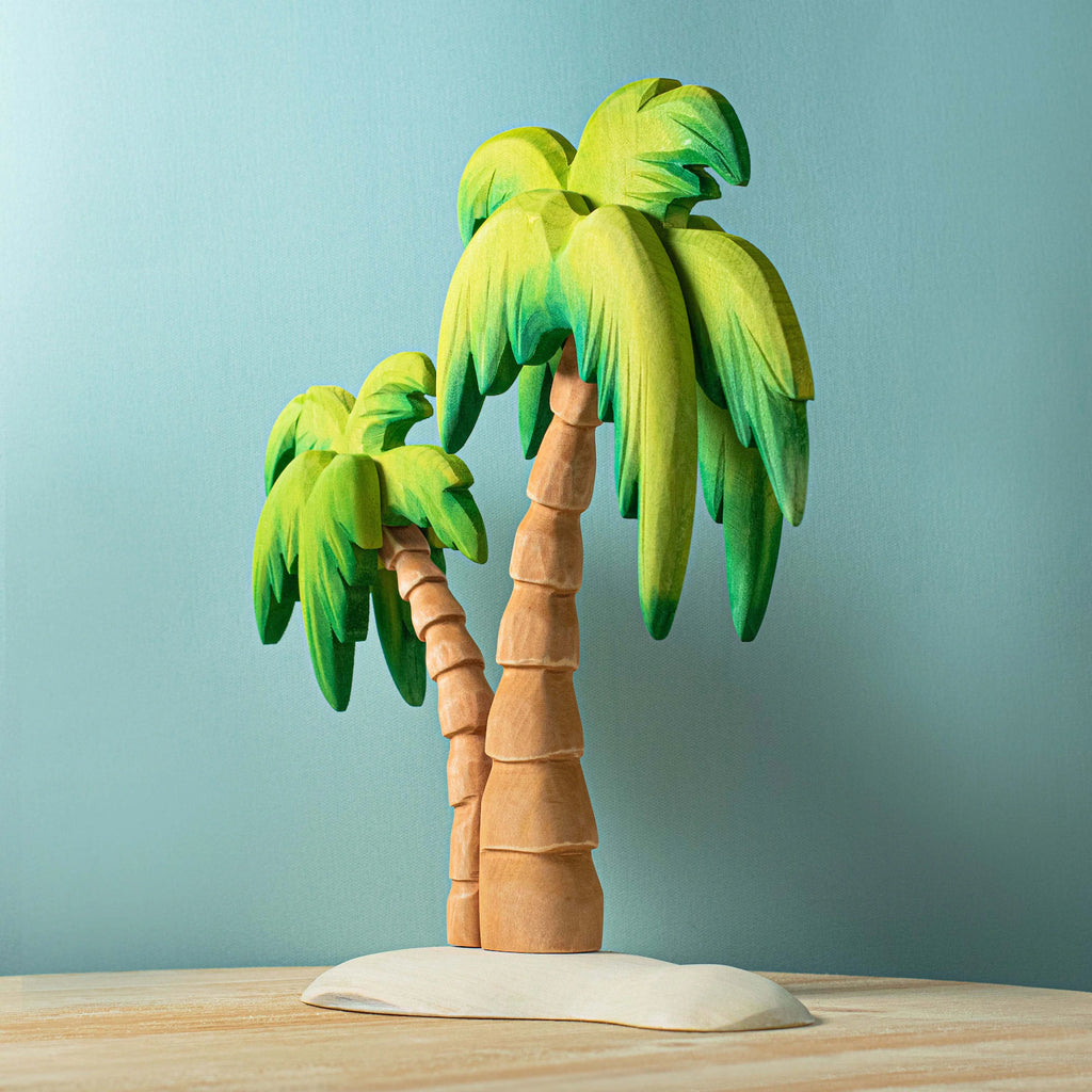 A handmade model of two palm trees with brown trunks and green leaves on a sandy base, crafted from Set of Handmade Wooden Palm Trees & Waves, set against a plain light blue background.