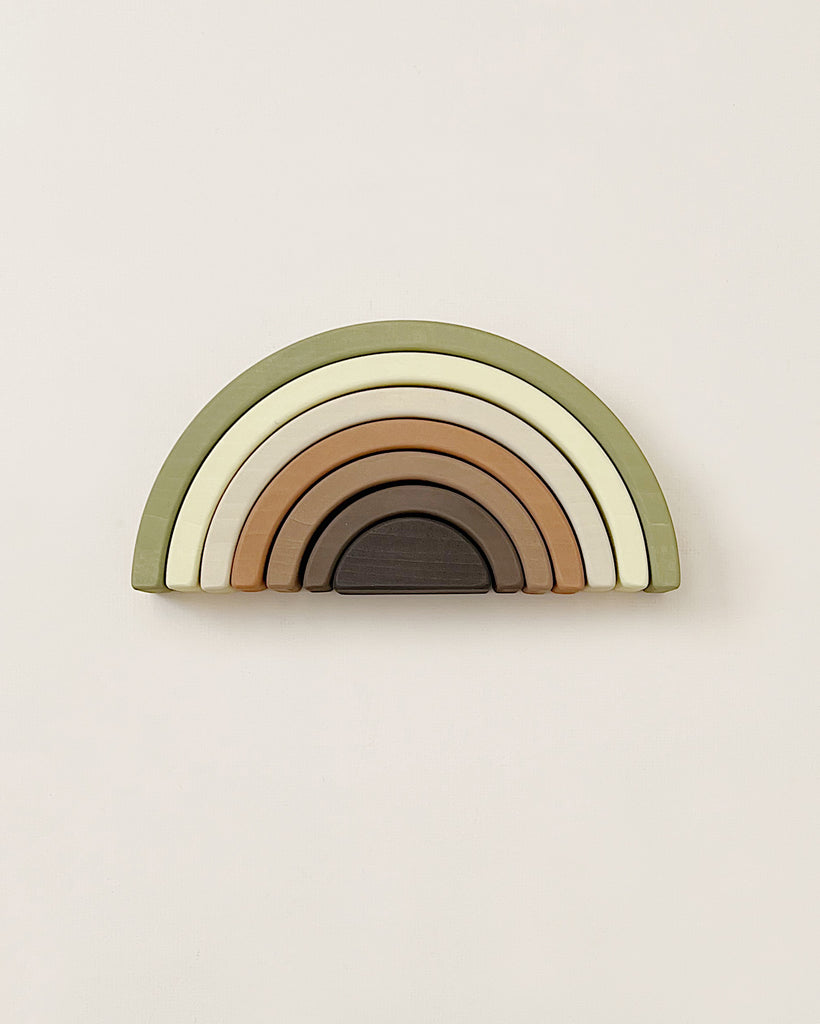 The Handmade Rainbow Stacker - Olive is designed in the shape of a rainbow with arches in various earthy tones, from outer to inner: olive green, light green, cream, tan, brown, and dark brown. The toy features non-toxic paint and is set against a plain, light background.