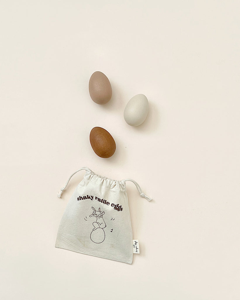 Canvas bag that says "shaky rattle eggs". 3 wooden eggs in natural, light brown and dark brown colors. 