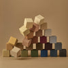 A collection of Raduga Grez Small Cube Blocks painted with non-toxic paint in various muted colors, forming an asymmetrical structure on a beige background.