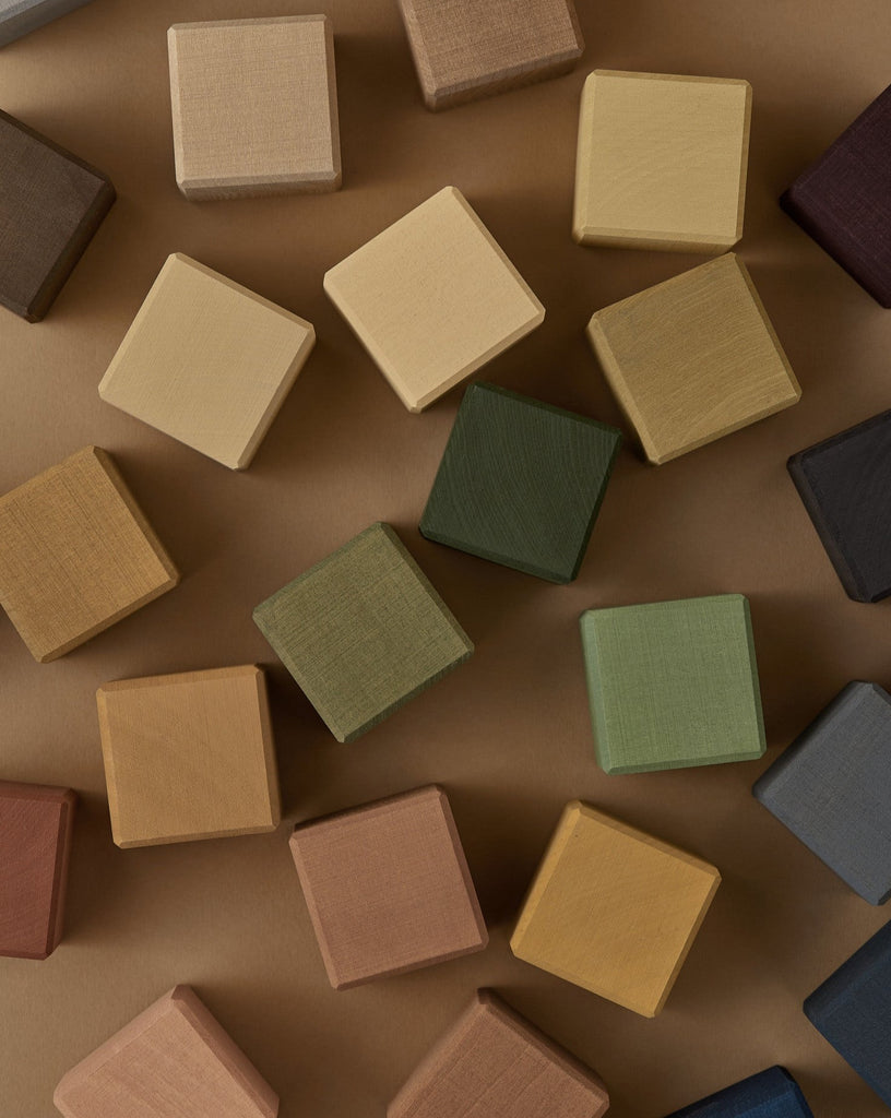 Raduga Grez | Small Cube Blocks arranged neatly on a brown background, showcasing a variety of earthy tones like tan, green, and burgundy, all finished with non-toxic paint.