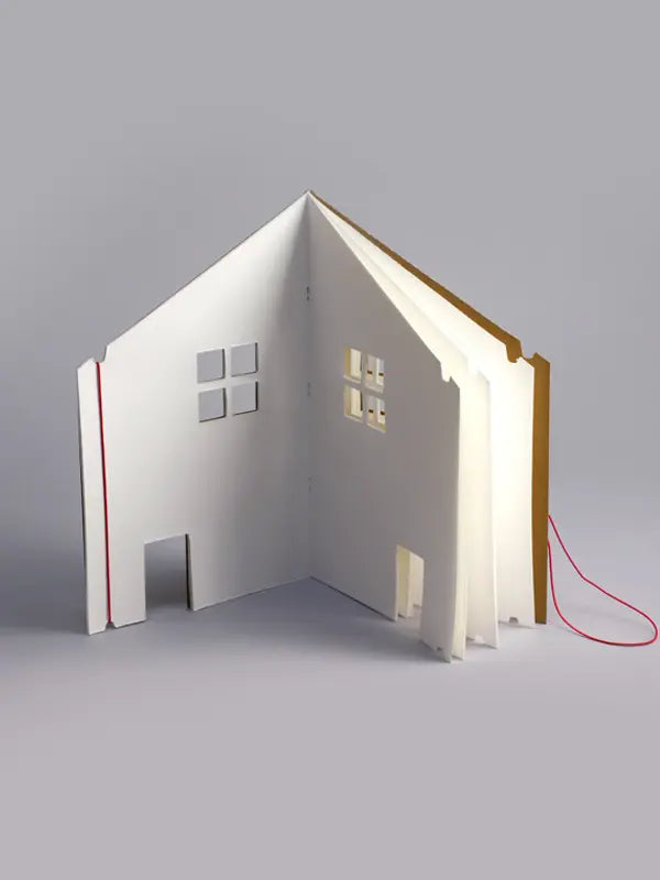 A Dollhouse Drawing Book model of a house, partially open like a book, with a red binding and a light illuminating some windows from the inside.
