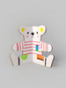 A colorful paper craft of a teddy bear with a striped red and white shirt, featuring multicolored patches on the body, arms, and ears, set against a plain gray background from The Teddy Bear Drawing Book.