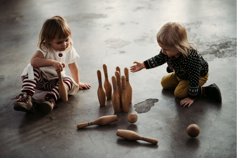Children sitting on the floor playing with wooden bowling set.