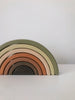 A Handmade Rainbow Stacker - Olive displays seven semicircular arches in muted earth tones, ranging from dark brown at the base to light green at the top. Painted with non-toxic paint, the toy is set against a plain white background.