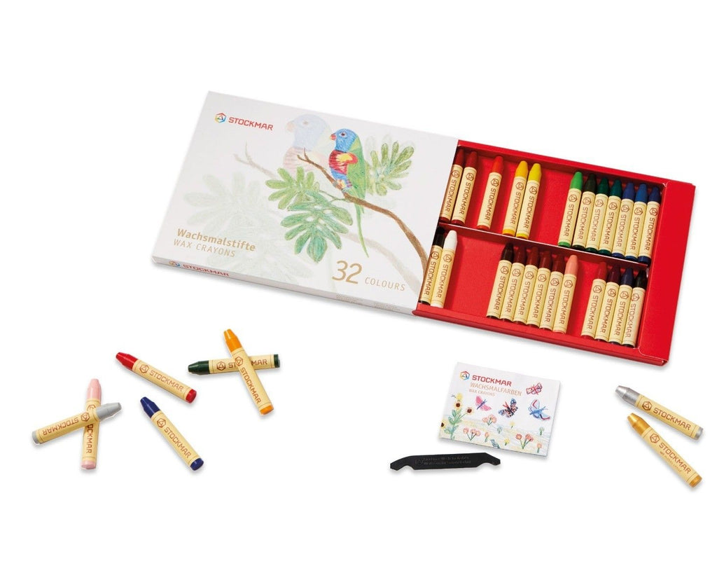 A set of 32 vibrant Stockmar Wax Stick Crayons Box - 32 Assorted displayed both in an open red box and scattered around it, with a sharpener and packaging depicting a parrot on a branch.