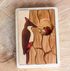 A Handmade Double Layer Wooden Puzzle - The Nest on a tray, featuring pieces that come together to form a colorful woodpecker perched beside a flower, set against a curved textured background.