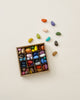 A small square box filled with colorful, Non-Toxic 64 Piece Crayon Rocks neatly arranged in compartments, with a few scattered crayons outside the box on a light background.