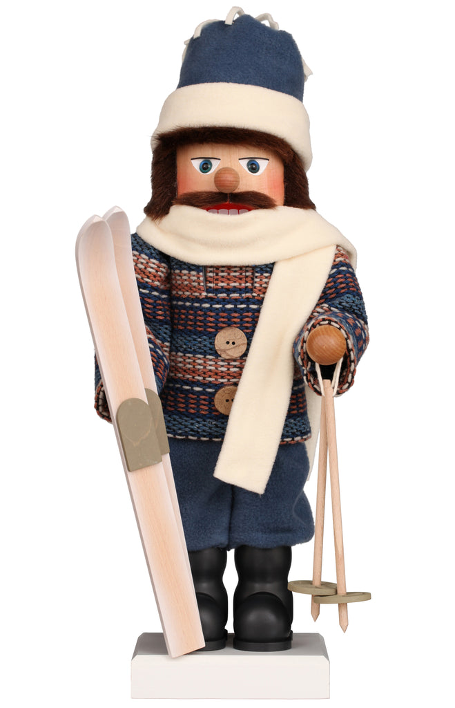 The Christian Ulbricht Collectible Wooden Nutcracker - Skier is a limited-edition German-made figurine dressed in winter clothing, complete with a blue patterned sweater, matching hat, and white scarf. It holds a pair of skis and poles and stands upright on a white base, showcasing the expert craftsmanship typical of Christian Ulbricht nutcrackers.