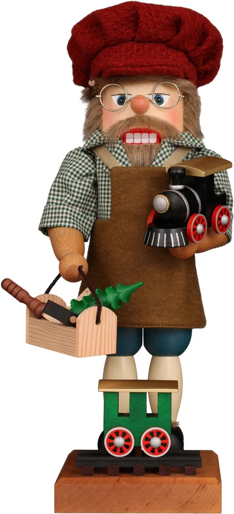 The Christian Ulbricht Collectible Wooden Nutcracker – Railroad Builder Limited Edition 2500 features glasses, a red hat, an apron, and holds a toy train and crate of vegetables while standing on a base with a green train car.