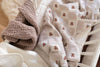 A close-up of cozy, folded Organic Cotton Baby Blanket - Teddy draped over a white crib, featuring a textured brown organic cotton blanket and a soft cream blanket with a teddy bear pattern.