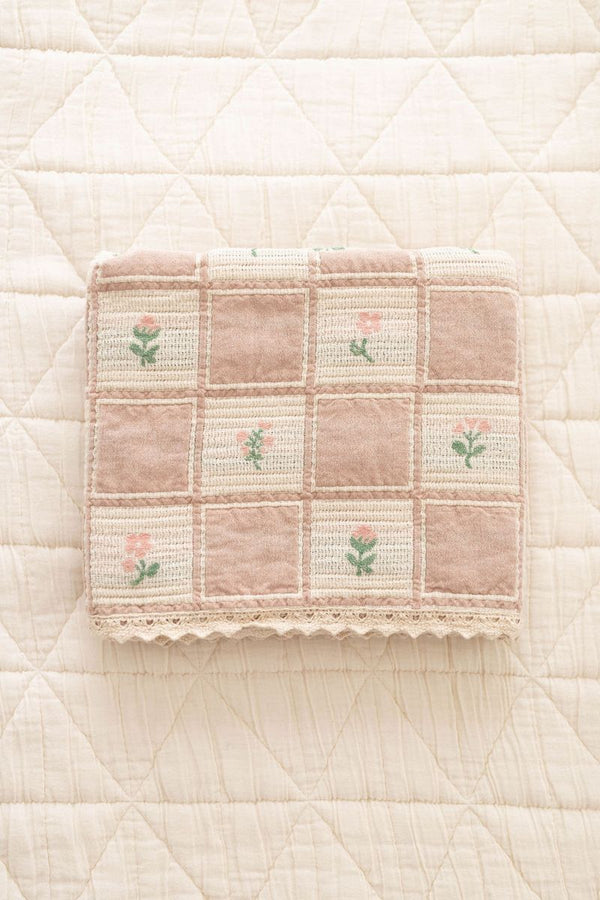 The Organic Cotton Baby Blanket - Fleur features a patchwork design with pink and green embroidered flowers, made in Portugal from organic cotton, shown on a cream quilted surface.