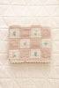 The Organic Cotton Baby Blanket - Fleur features a patchwork design with pink and green embroidered flowers, made in Portugal from organic cotton, shown on a cream quilted surface.