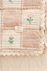 A close-up of the Organic Cotton Baby Blanket - Fleur shows its pink and cream checks, delicate embroidered flowers, lace trim, and a "NEVERFAIN" label. Made in Portugal from organic cotton.