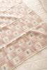 The Organic Cotton Baby Blanket - Fleur is a soft, pink and cream patchwork blanket with a grid pattern and small green and pink floral designs, shown draped over a light quilted surface.
