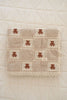 The Organic Cotton Baby Blanket - Teddy is a beige, quilted blanket with lace trim and a grid pattern featuring brown teddy bears, neatly folded on a cream quilt. Made in Portugal from soft, high-quality organic cotton.