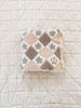 The Organic Cotton Baby Blanket - Prairie, featuring a pastel diamond and flower pattern, is folded atop a cream-colored quilted surface with a simple grid design.