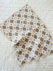 The Organic Cotton Baby Blanket - Prairie features a handmade checkered pattern in cream, beige, brown, and blue-gray with some blue-gray floral designs—ideal as a cozy baby blanket on any bedspread.