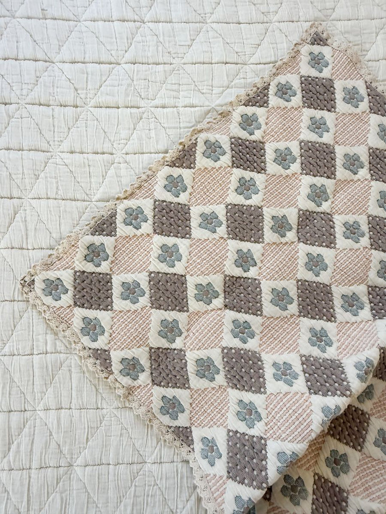 The Organic Cotton Baby Blanket - Prairie, featuring a diamond pattern in beige, cream, and gray with blue floral accents, is folded on a cream quilted backdrop. Expertly crafted in Portugal from organic cotton.
