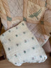 Two vintage quilts are draped over a checkered chair. One is the Organic Cotton Layered Gauze Blanket - Dahlia, crafted from organic cotton in pale pink and adorned with green and pink floral designs. The other quilt is off-white, featuring a delicate rose pattern, scalloped edge, and a soft 8-layer gauze texture. A wooden floor is visible in the background.