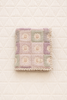 The Organic Cotton Quilt - Sundrop, crafted in Portugal from organic cotton and featuring a pastel patchwork design with floral patterns and delicate lace trim, is displayed on a white, quilted background.