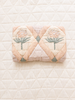An Organic Cotton Quilt - Granny, featuring a pink and green floral pattern, is folded and placed atop a larger cream-colored quilted blanket with a diamond design.