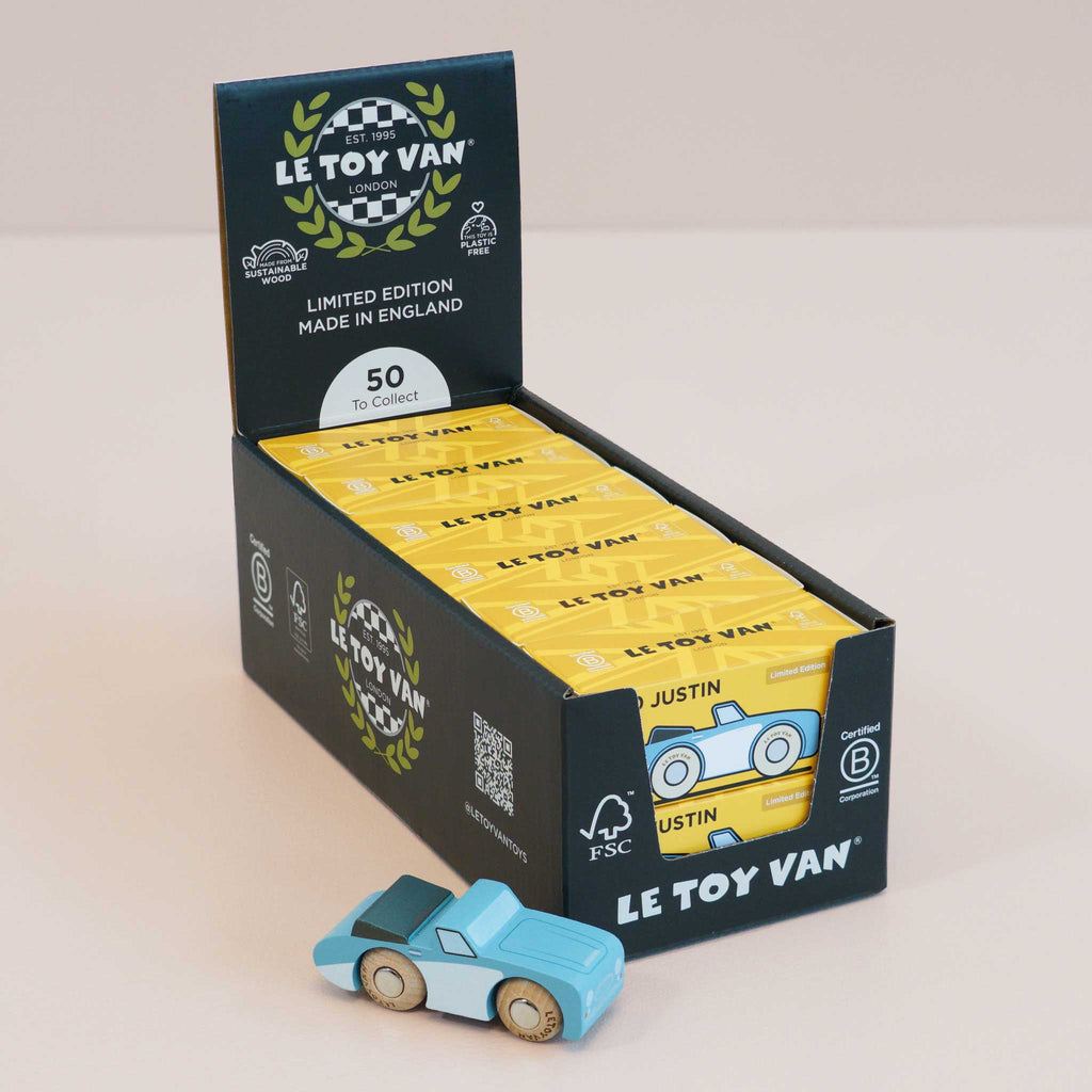 A display box labeled “Le Toy Van” holds several yellow packages, showcasing the No. 1 GT10 Justin | Made in England—a charming wooden car and classic keepsake—placed in front. The box highlights “Limited Edition,” “Made in England,” and notes that there are “50 to Collect.”.