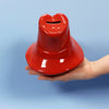 A hand holds the Paddington Money Bank, a glossy red ceramic coin bank shaped like Paddington Bear's hat with a coin slot on top, set against a light blue background.