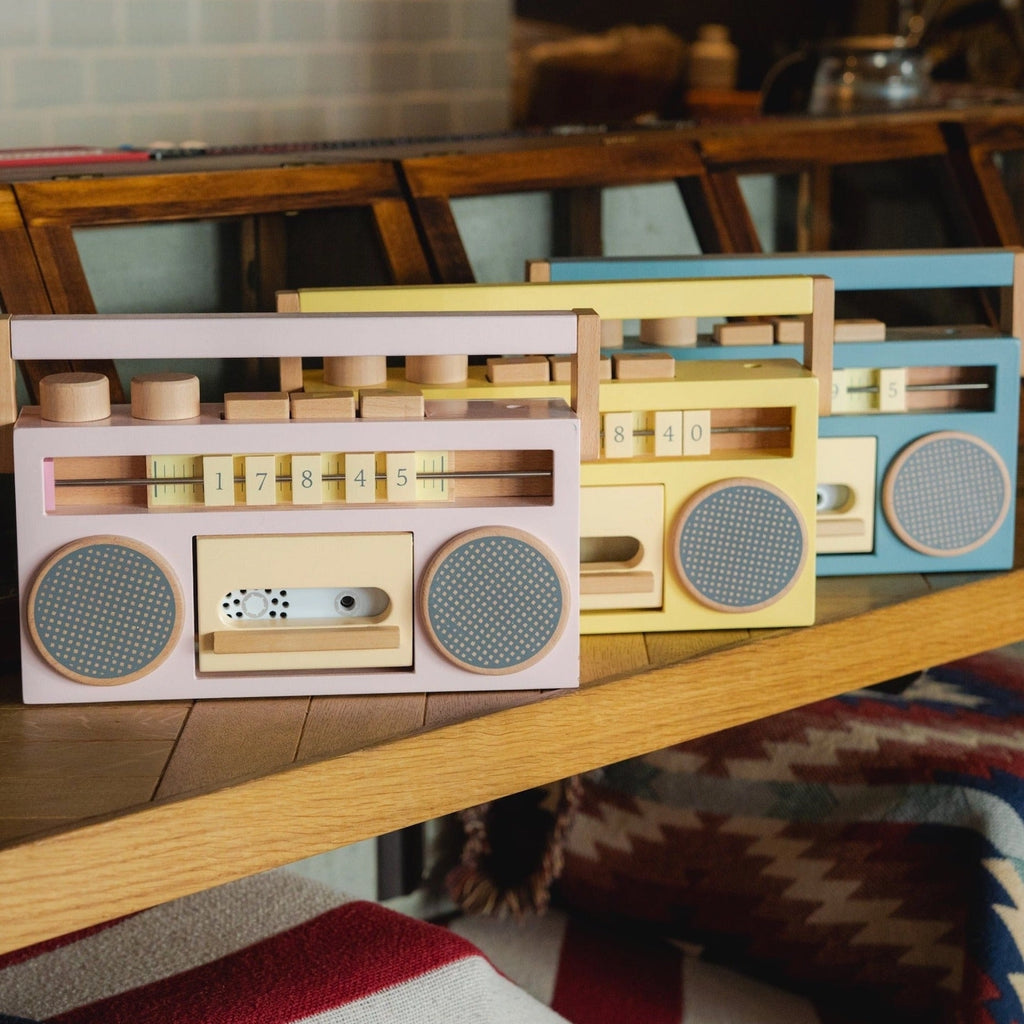 A collection of four colorful Retro Wooden Tape Recorders displayed on a wooden shelf, each in pastel shades of pink, blue, yellow, and cream, including an old school boombox with visible knobs and speakers