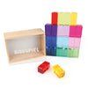 A set of colorful, translucent educational Bauspiel Luminous Blocks - 24 Piece forms a pyramid next to a wooden "Bauspiel" box, with two blocks at the front, all on a white surface.