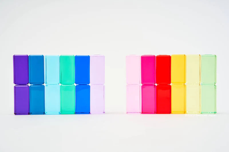 Two rows of colorful, transparent Bauspiel Luminous Blocks are displayed. The left set includes blue and purple blocks, while the right features red, pink, yellow, and green. Designed as high-quality educational building sets, they stand against a plain light background.