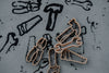 Four sustainable playdough cutters from the Tools Cutter Set - Eco Playdough Tool—featuring shapes of a plier, saw, wrench, and hammer—are arranged on a surface with matching black tool outlines printed beneath them. This eco-friendly set is ideal for creative, tool-themed play.