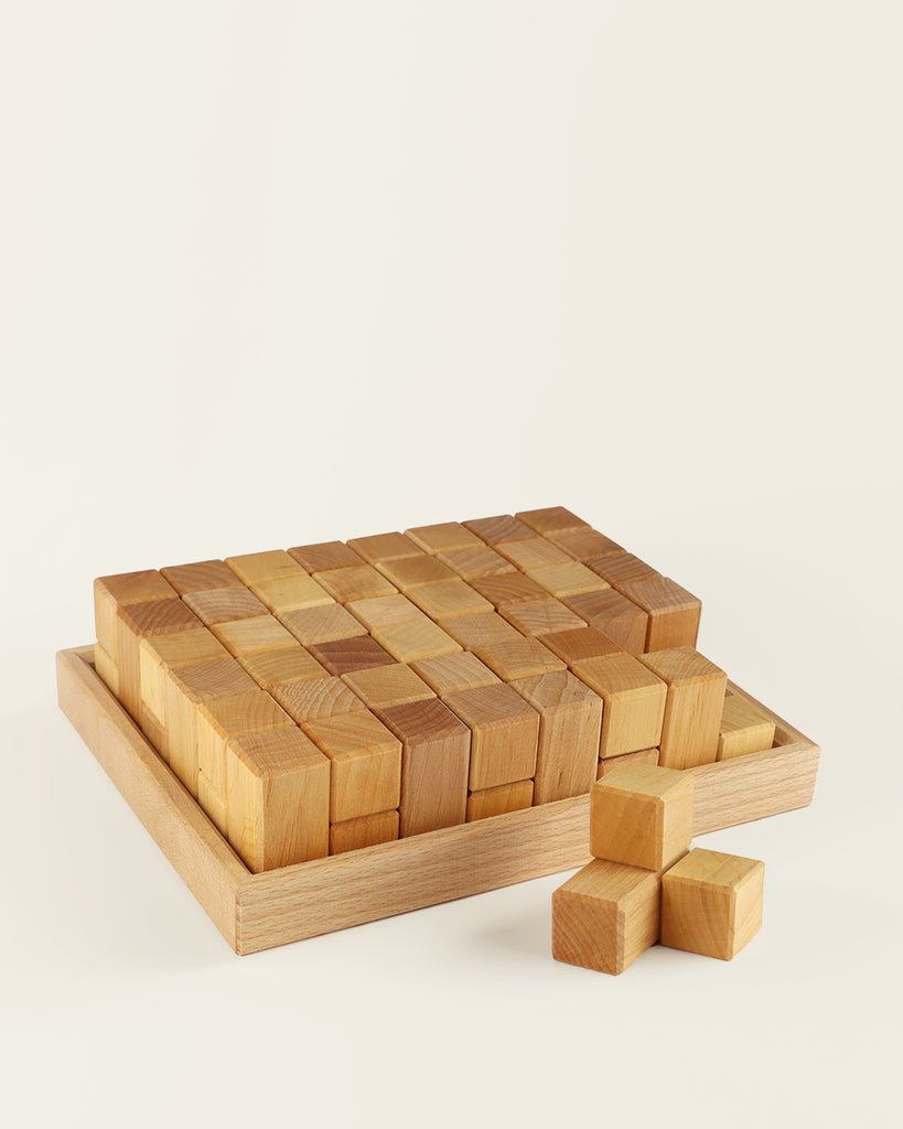A set of Bauspiel Natural Corner Blocks, 24-Piece Set in a shallow tray, with three additional blocks arranged in a small stack nearby.