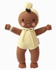 Cuddle + Kind My First Baby (Buttercup) is a hand-knit brown baby doll made from natural cotton yarn, dressed in a cream romper with hood and pom-pom, rosy cheeks, and open arms. Ships in one week.