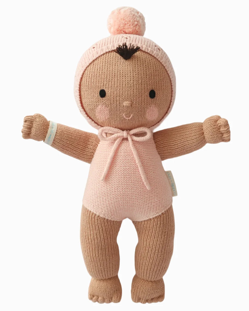 Cuddle + Kind My First Baby (Peach) ships in one week. This fair trade, hand-knit doll has brown skin, a simple embroidered face, outstretched arms, and comes dressed in a pink outfit with a matching pom-pom hat. Made from natural cotton yarn.