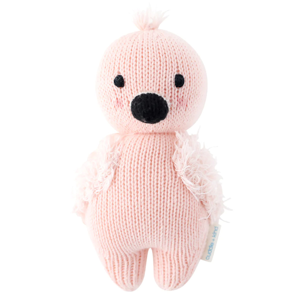 A pink hand-knit Cuddle + Kind Baby Flamingo plush toy, featuring a black nose and tufts of yarn as ears, isolated on a white background.