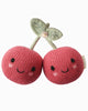 The Cuddle + Kind Baby Cherry features two pink knitted cherries with smiling faces, blushing cheeks, and green hand-knit stems with leaves, all beautifully handcrafted in a plush style from heirloom-quality natural Peruvian cotton yarn.