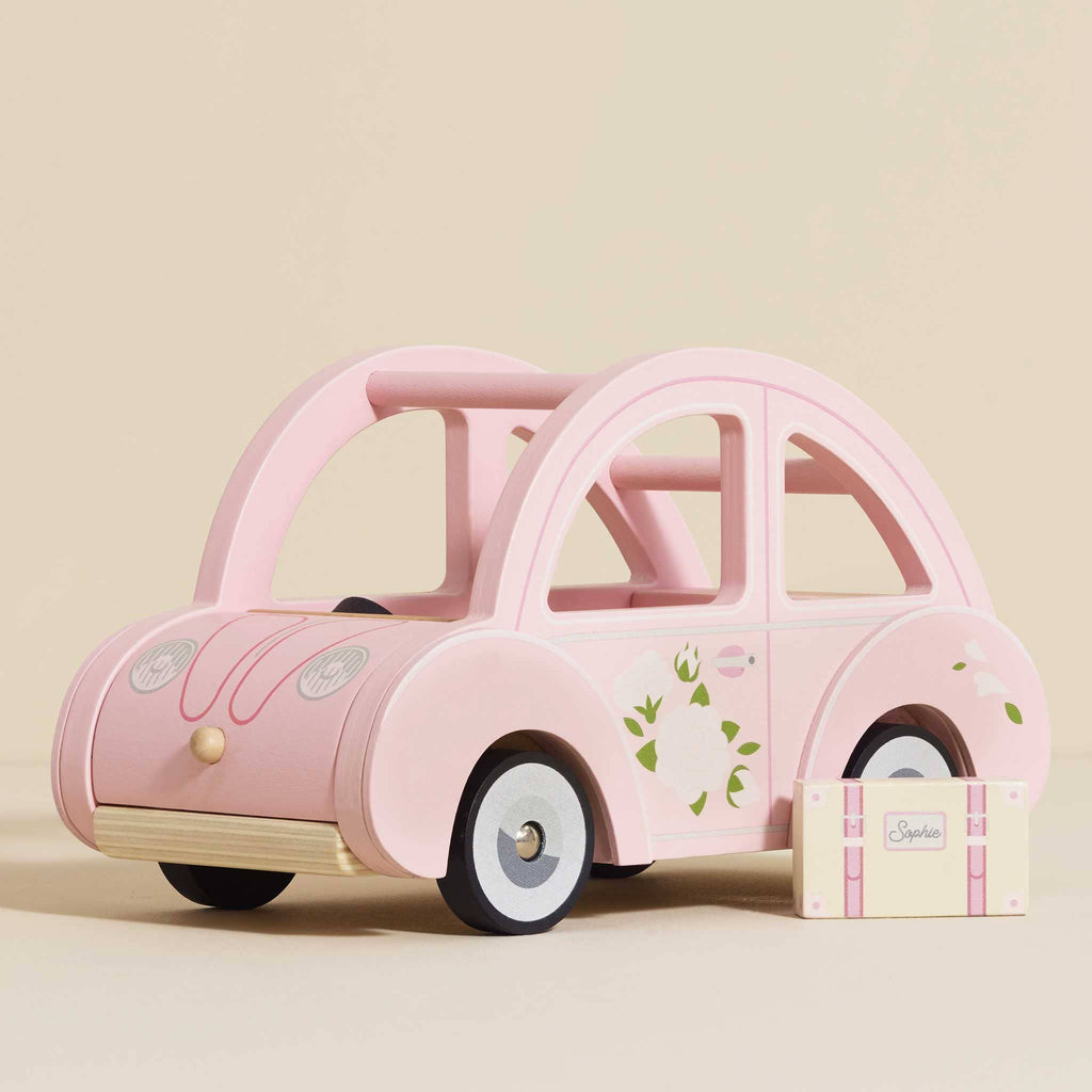 Sophie's Dolls House Toy Car—a pink retro wooden car with floral designs—sits beside a matching "Sophie" suitcase on a beige background, ideal as an educational toy or charming nursery decor.
