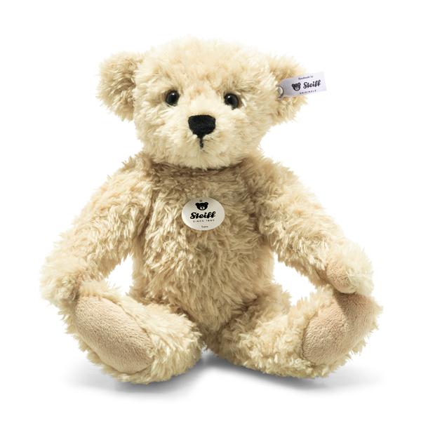 A 12-inch Steiff Luca Teddy Bear, light brown and plush with black eyes, a black nose, and the signature Steiff "Button in Ear" tag in its left ear, sits upright with arms open and legs slightly spread.