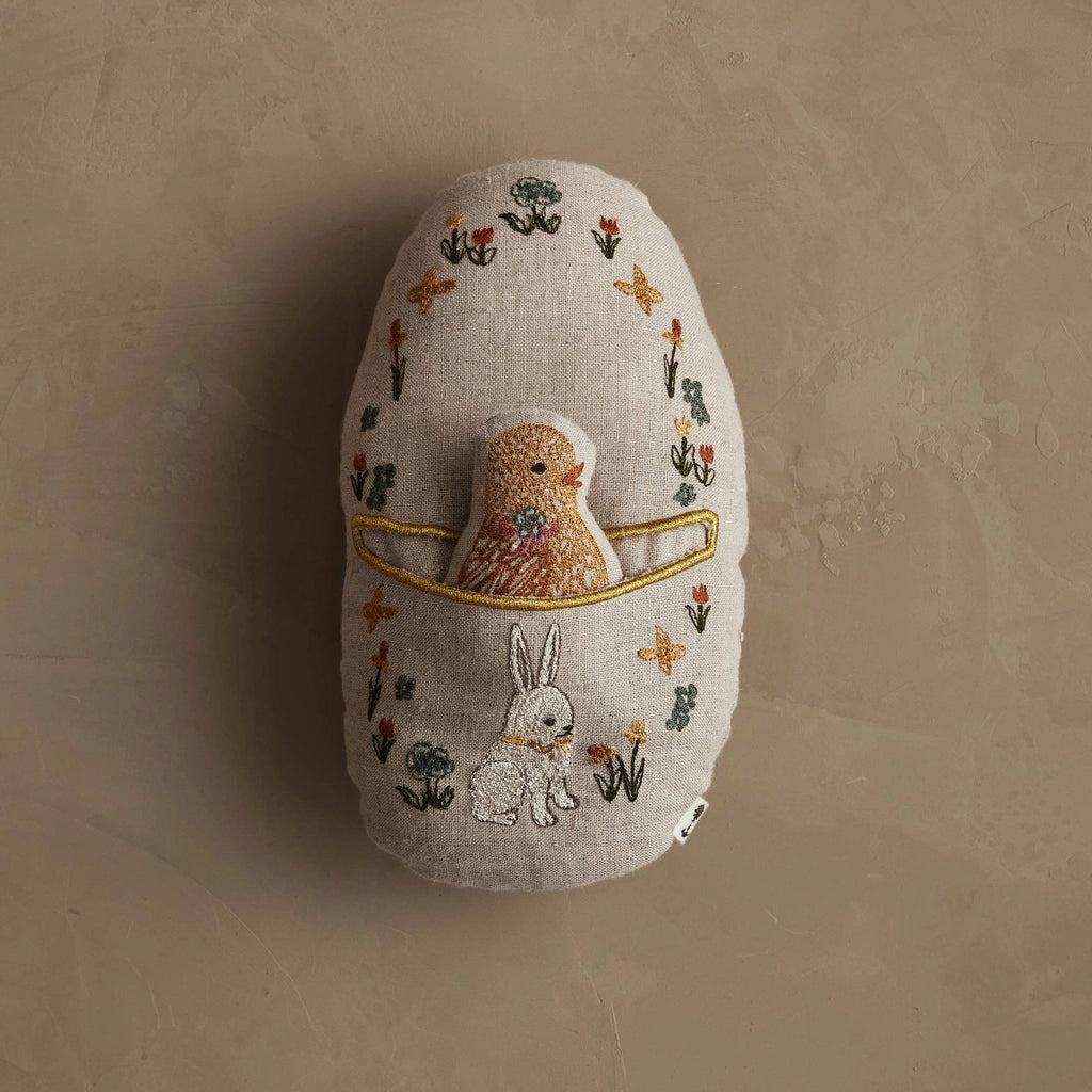 The Coral & Tusk Pocket Easter Egg is a soft, oval-shaped beige pillow with an embroidered yellow chick in the center, flowers, and a white bunny at the bottom—perfect for any Easter basket.