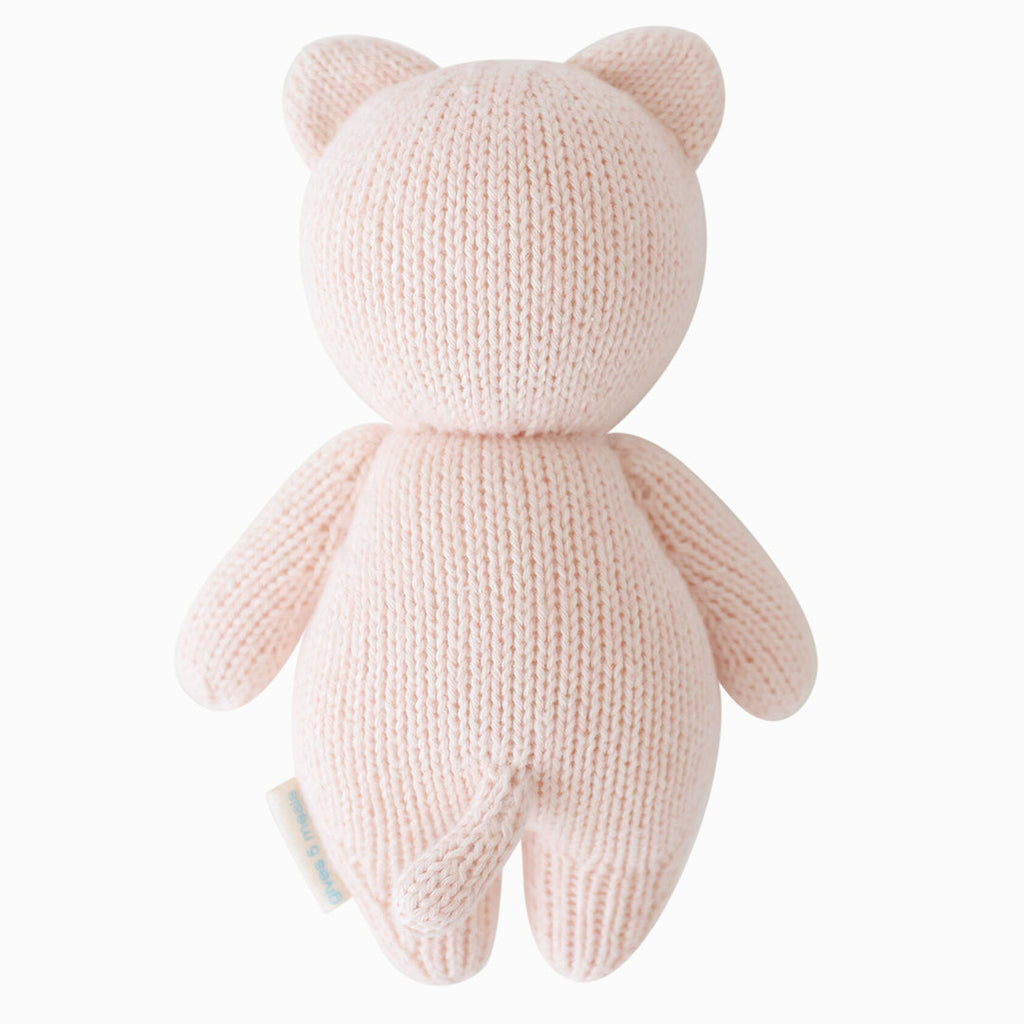 The Cuddle + Kind Baby Kitten (Blush) is a soft, blush pink hand-knit plush made from Peruvian cotton yarn, shown from the back with round ears, a small tail, and outstretched arms—ideal for fans of heirloom dolls and hand-knit baby animals.