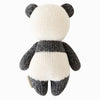 The Cuddle + Kind Baby Panda is hand-knit with a black and white striped body on a plain white background. Made from Peruvian cotton yarn, the toy features a simplistic design with visible stitching and textured yarn.